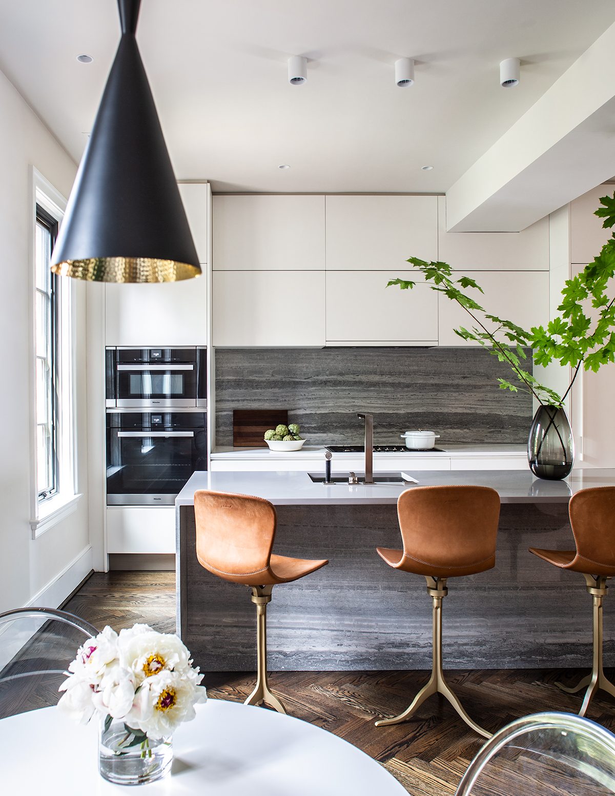 Modern kitchen with a stone-wrapped island, three leather stools, and a black pendant — Cleveland Park Residence by Christopher Patrick Interiors