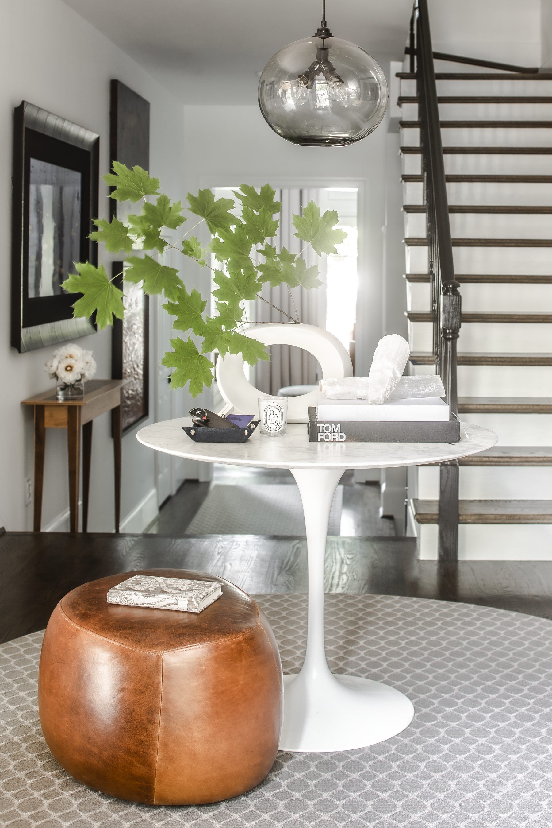 Entry with a tulip table, leather pouf, and a smoked-glass pendant by the stair — Cleveland Park Residence by Christopher Patrick Interiors