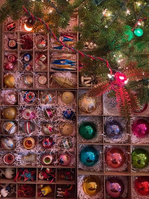 Boxes of vintage glass Christmas ornaments beside a lit tree — holiday decorating by Christopher Patrick Interiors