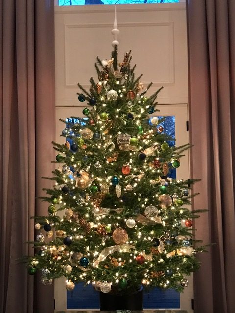 Christmas tree with gold and copper ornaments in front of a tall window — holiday decorating by Christopher Patrick Interiors